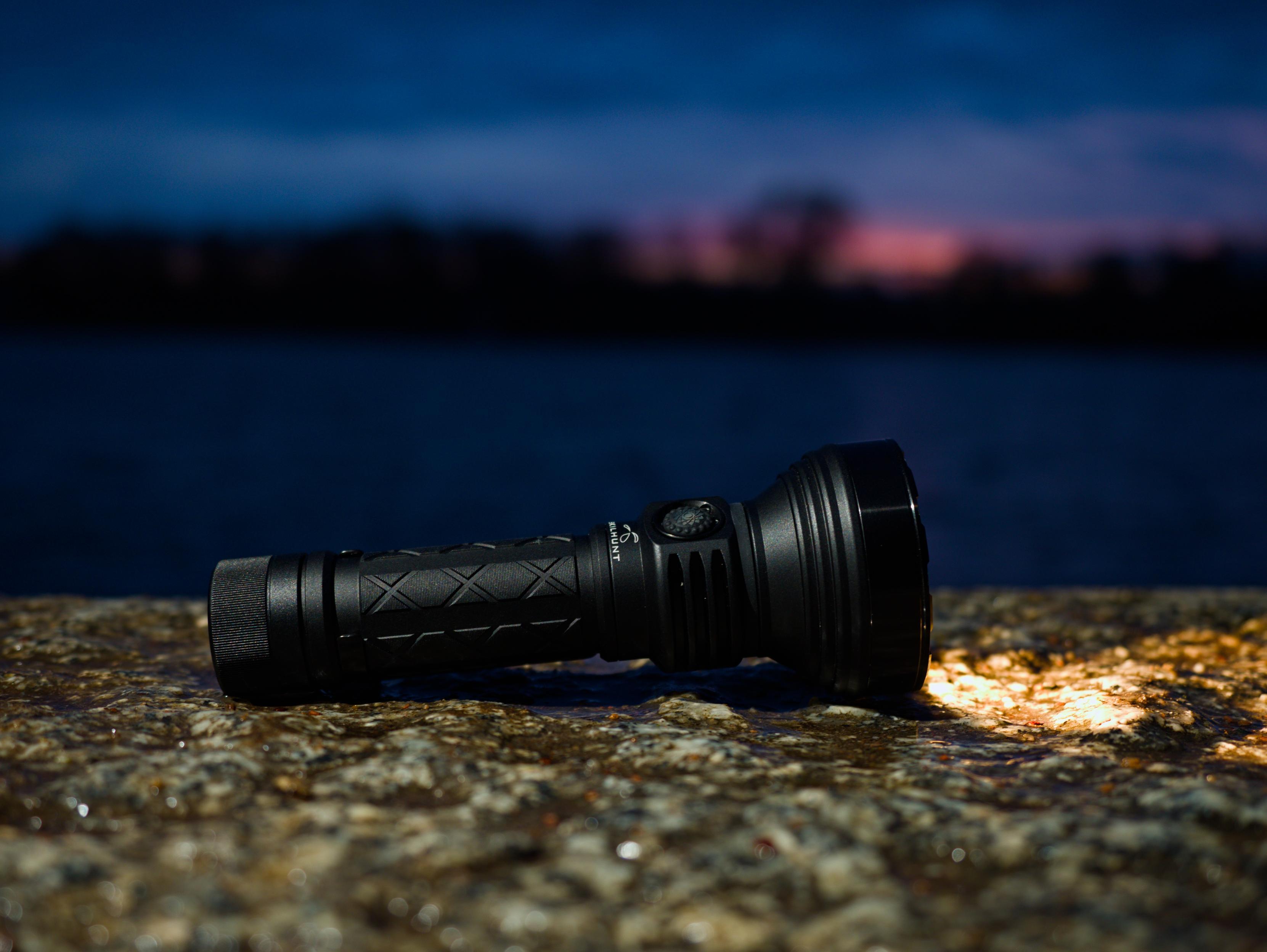 A Skilhunt EC500 flashlight on a stone wall with a body of water and sunset in the background