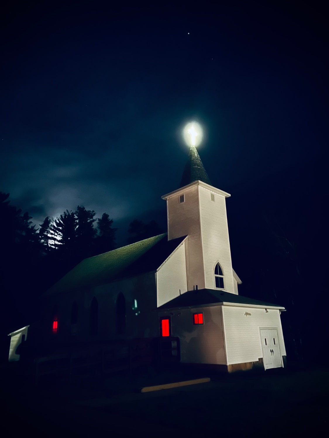 Photo of a white church at night. The windows are glowing with an ominous red light